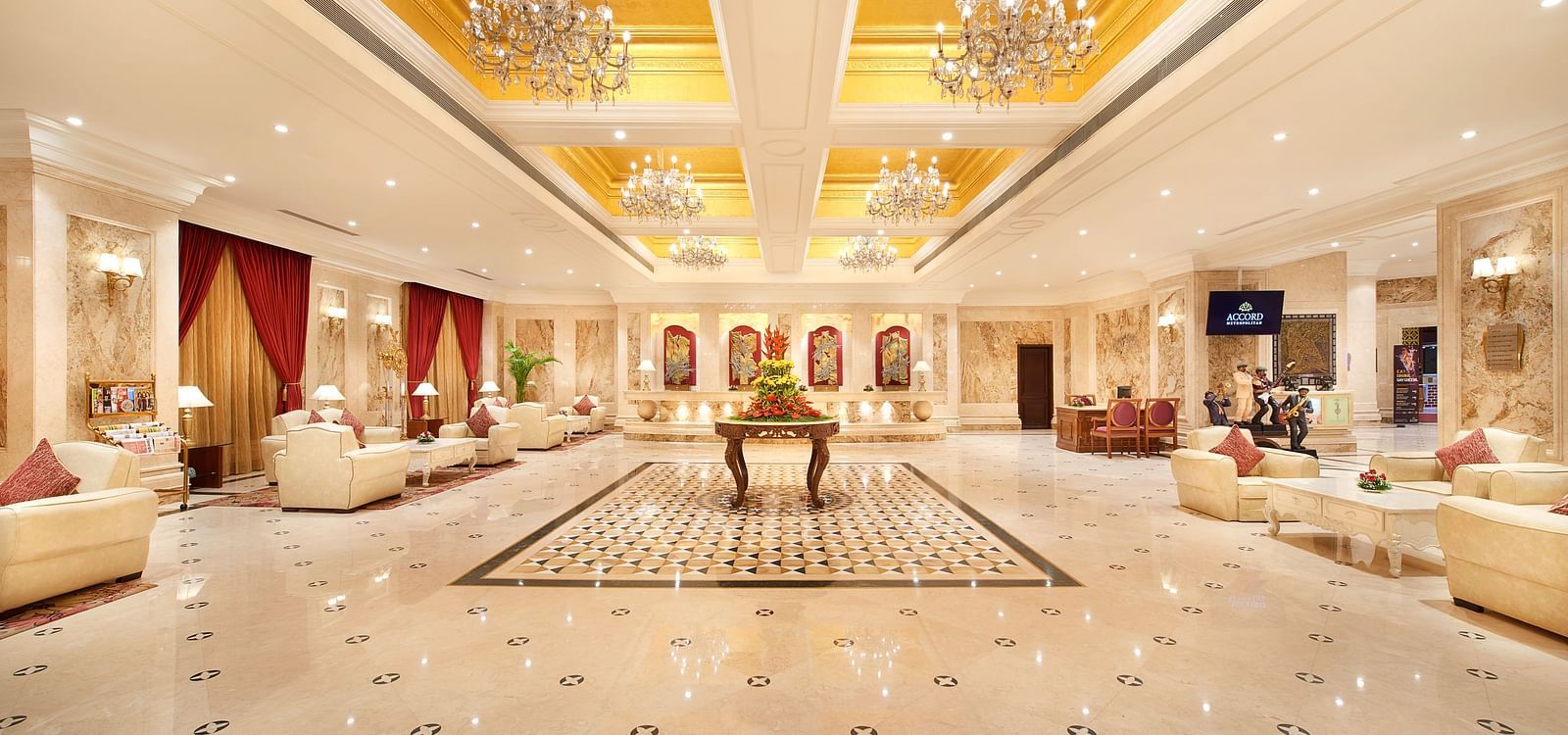 Spacious lobby at Accord Hotels and Resorts with luxurious interiors, wooden tables, cushioned furniture, chandeliers, and warm lighting.